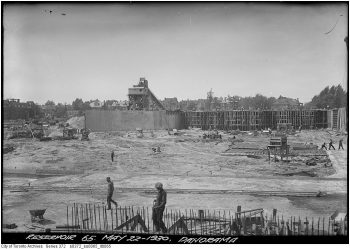 Workers erect tall concrete forms on bare earth.