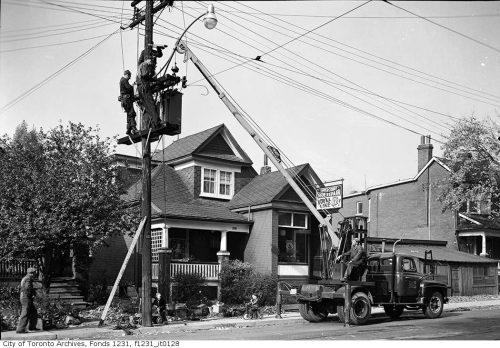 Workers use a crane truck to reach a streetlight in a residential area.