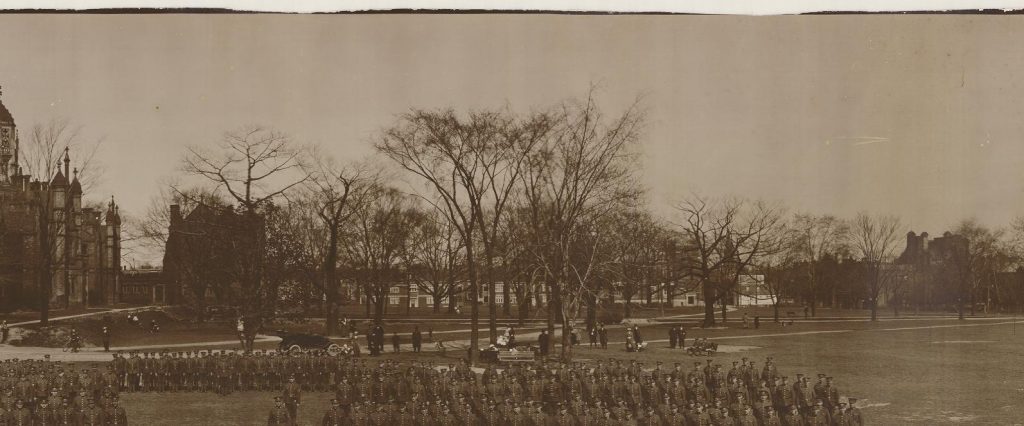 Men in armed forces uniforms lined up in the grounds of a large school.