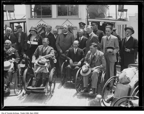 Group of men in wheelchairs or standing on the deck of a ferry boat.