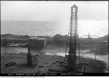 Construction materials stacked on a bare area near the lake beside a vertical conveyor belt.