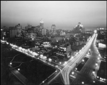 The city see at night from above, with buildings lit up and the roads showing as streams of light.