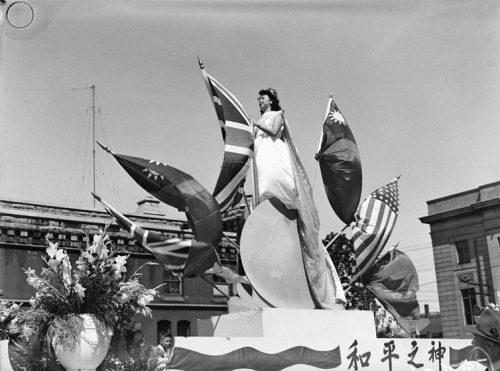 A Chinese woman stands on a parade float surrounded by flags.