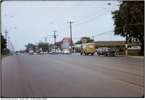 Cars driving past motels and a restaurant with bright signs.