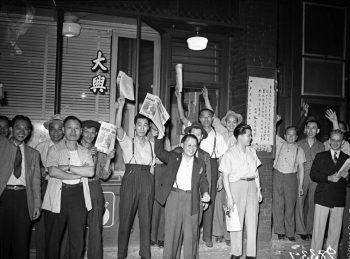 Chinese men in front of a storefront hold up newspapers.