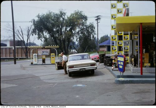 Man getting out of a car in front of a bright yellow gas station building.