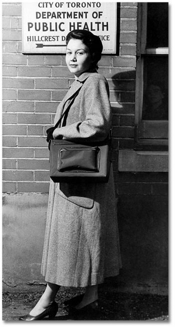 Woman in long coat, carrying large bag.