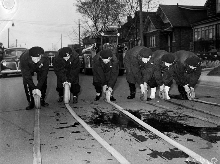 Women roll up long hoses on the ground.