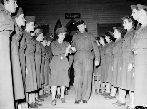 A woman and man in armed forces uniforms walk between rows of uniformed women.