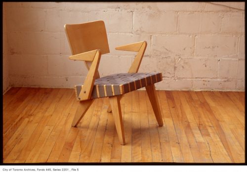 Blonde wood chair with triangular arms and black webbing seat.