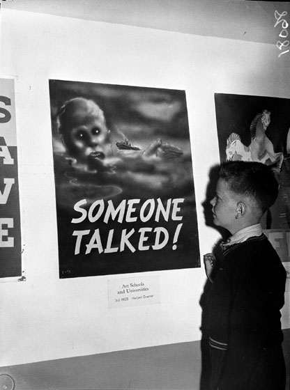 Boy standing in front of a poster showing a sinking ship and the words "someone talked".