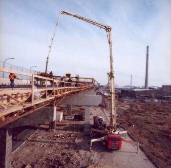 Red concrete truck has long crane-like arm that lifts hose up to deck of elevated expressway