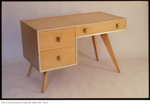 Blonde wood desk with angled legs and three drawers.