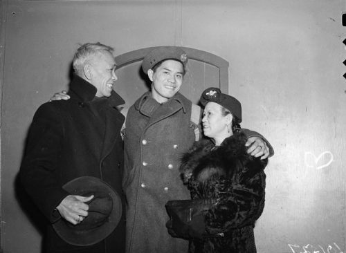 A Chinese Canadian man in military uniform has his arms around an older man and woman.