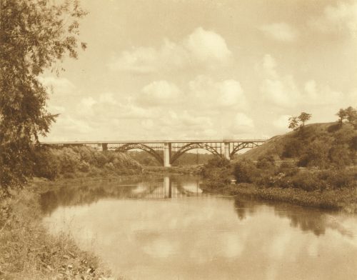 Viaduct with arched metal supports seen with river and trees in the foreground.