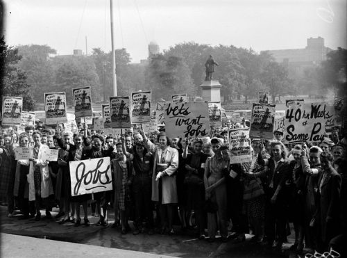 A large crowd holds up signs with slogans including 'Vets want jobs' and 'Make wartime factories give peacetime jobs' and '40 hour week & same pay.'