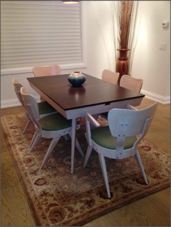 Dining room with table with dark top and white chairs with green seats.