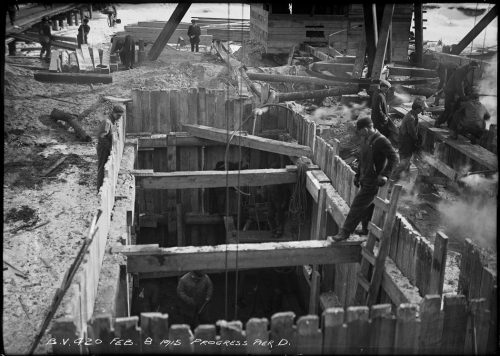 Workers in excavated pit lined with wooden supports.