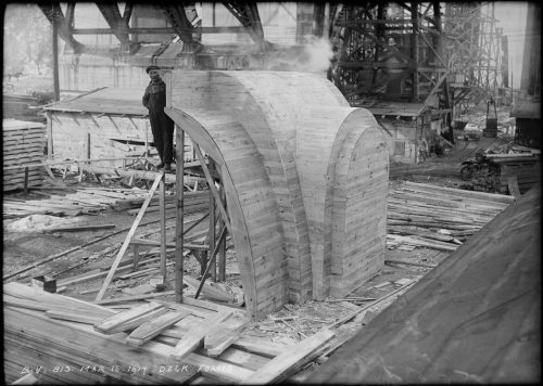 Man standing beside arch-shaped wooden mould twice as tall as he is.