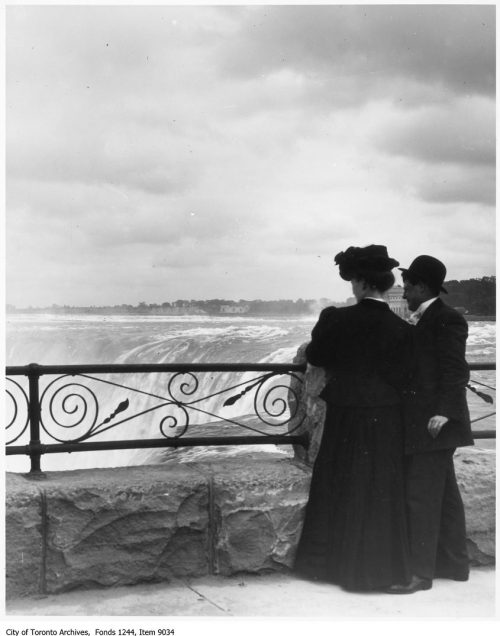 Two people look over a wrought iron fence to Niagara Falls.