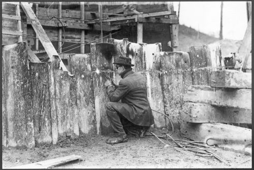 Man burning a straight line through a line of metal slabs that are uneven at the top.