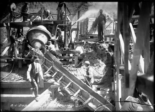 Cluttered, busy construction site with excavated earth, a concete making machine and wooden moulds.