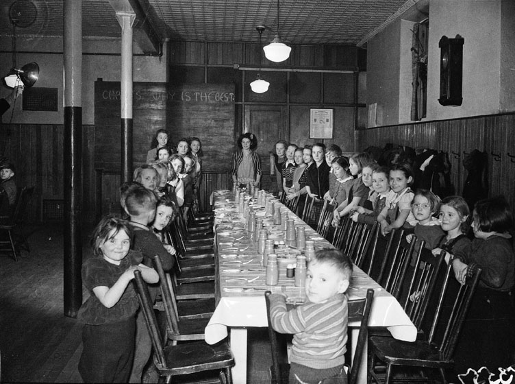 Children standing behind chairs at a long dinner table.