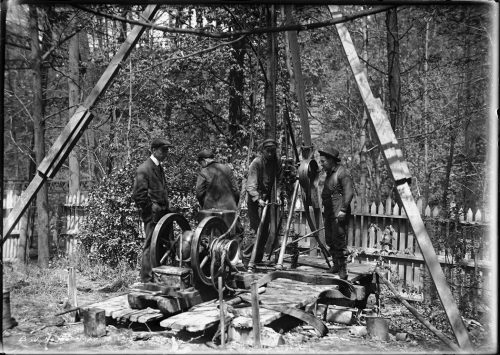 Men operating a machine with wheels under a large wooden tripod.