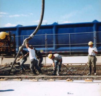 Workers guide concrete from overhead hose onto roadbed
