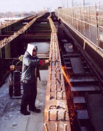 Worker in protective glasses uses cutting torch to cut through thick metal beams