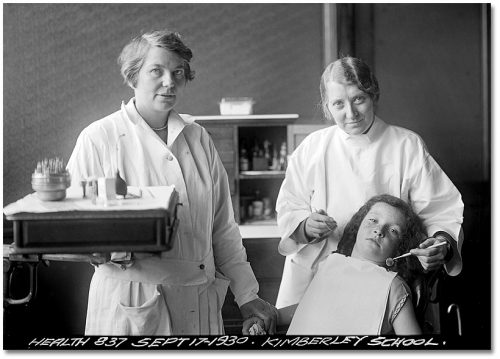 Two women who are dentists stand over a girl in a dentist's chair.