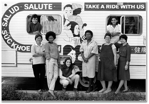 Women of colour and of different ethnicities stand in front of a trailer that is painted with Hello in various languages.