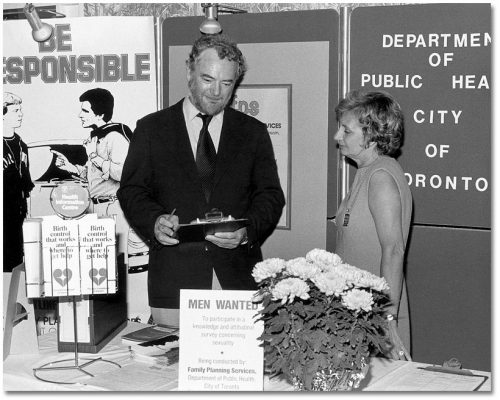 A man and woman stand in a booth that displays informational posters and brochures about birth control.