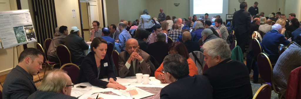 A room full of people seated around tables and discussing materials on the table.