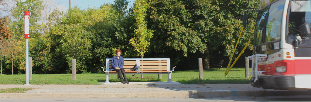 Image of an older lady waiting on a bench for a TTC bus