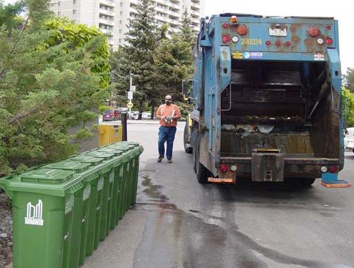 Collection truck and worker in front of a row of new Green Bins