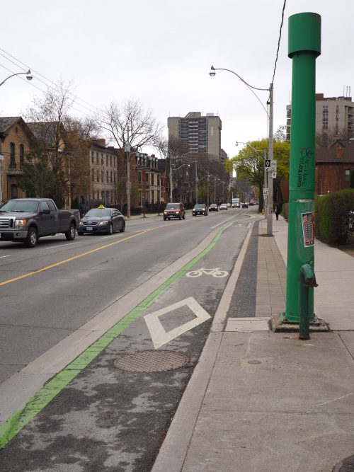 Sherbourne Cycle Track looking south - A raised bicycle lane includes a diamond, bicycle symbol and green paint to separate it from one lane of motor vehicle traffic.