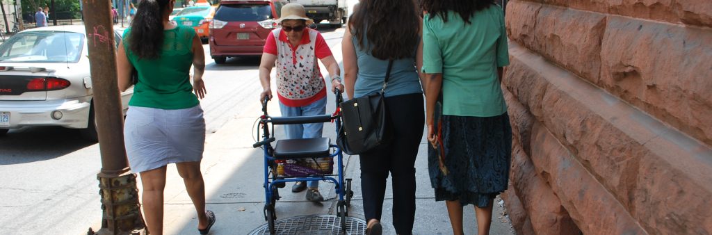 Image of an older lady walking on the sidewalk with a walker