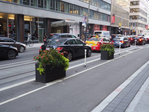 Richmond St W Cycle Track - a bicycle lane is separated from motor vehicle traffic by planters and bollards.