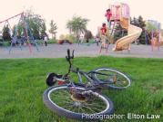 A child leaves their bicycle on the ground and goes to play on a slide at a playground.