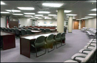 View of Committee Room 1, where you can see chairs set up along the back wall, with a table and chairs facing the front of the room, and a three rows of long desks set up in a type of horseshoe formation.
