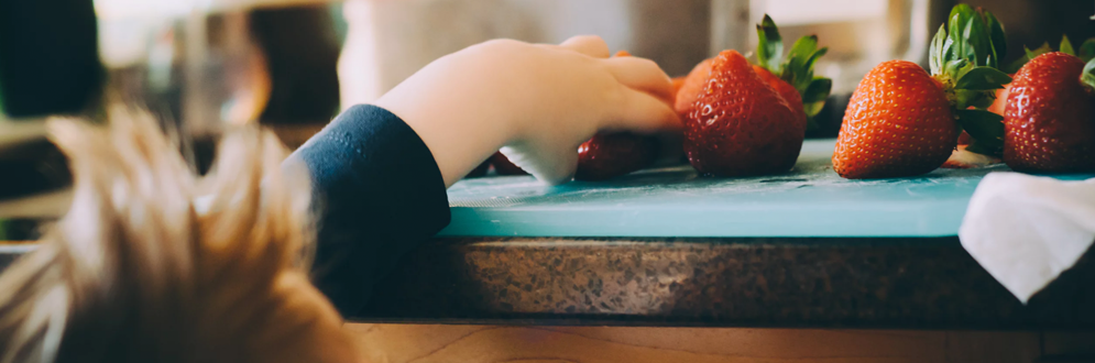 Boy reaching on the countertop for strawberries