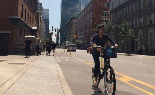 Image of cyclist using designated bike lane and wide sidewalks on Simcoe Street. 