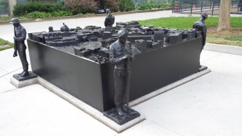 Peace Through Valour sculpture, which is a square sculpture with a soldier at each corner and the main square of the sculpture contains a city.