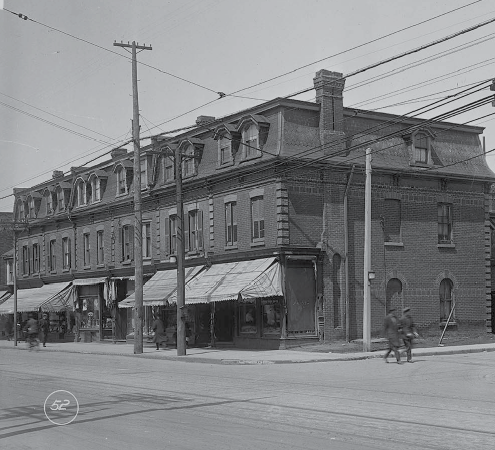 This is an archival photograph showing a row of buildings in the early 20th century at the corner of Queen Street West and Lisgar Street