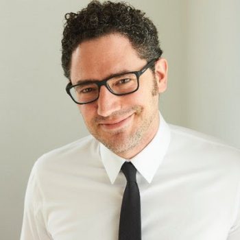 Photograph of Elan Mastai smiling, wearing glasses and a white dress shirt and black tie.