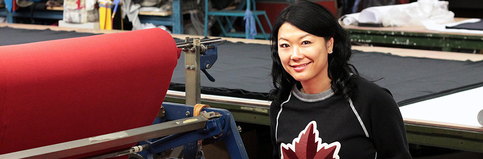 smiling woman standing beside a roll of fabric in a clothing factory