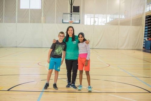 An instructor stands with a boy and girl on a basketball court