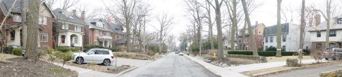 A residential street featuring a variety of houses with large front yards and mature trees.