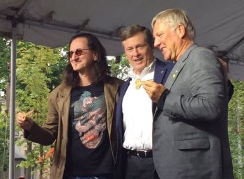 Two Rush band members hold up their keys to the City under a white tent with Mayor John Tory.